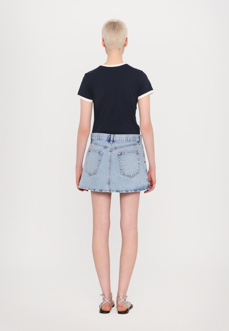 Marineblaues Kurzarmhemd mit weißem Besatz, kombiniert mit einem hellblauen Jeansrock. Der Rock hat eine ausgestellte Form und Rückentaschen. Schwarze Sandalen.