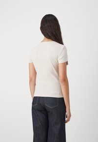 Fitted krem ribbestrikket T-skjorte med korte ermer, scoop-hals, og glatt tekstur, kombinert med høytlivde mørkeblå denim-bukser.