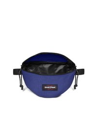 Modrá látková taška s černým interiérem a štítkem s logem. Má zipové uzavření a prošívané detaily. Kompaktní, zakulacený tvar.