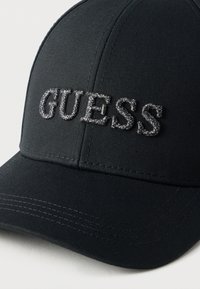 Μαύρο καπέλο από απαλό ύφασμα με κεντημένο λογότυπο "GUESS" σε ασημί κλωστή, δομημένο σχέδιο με καμπύλη γείσο.