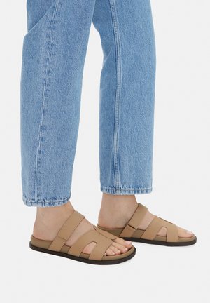 Sandali color tan con due ampie fasce incrociate e design con punta aperta, abbinati a jeans di denim celeste. Materiale liscio e suola piatta.