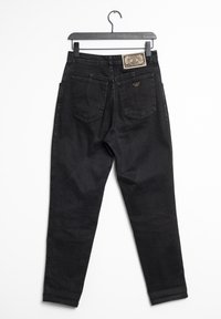 Svarta jeans hängande från en krok, med en etikett på midjebandet, två bakfickor och en tapered bendesign med minimal textur.
