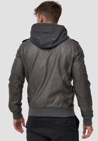 Chaqueta de cuero gris con una capucha de tela gris, puños y dobladillo acanalados, y acentos acolchados en los hombros. Presenta detalles de bolsillo en los lados.