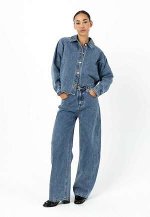 Spijkerjack met een klassieke kraag en knoopsluiting, gecombineerd met wijde spijkerbroeken, beide in lichtblauw met een subtiele textuur.