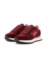 Une paire de baskets basses bordeaux et roses avec des semelles blanches et un logo géométrique sur le côté, lacées et légèrement inclinées vers la droite.