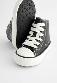 Schwarze Leder High-Top Sneakers mit weißer Gummikappe und -sohle, ausgestattet mit weißen Schnürsenkeln, Metallösen und einer schwarzen Sohle mit Sternmuster.