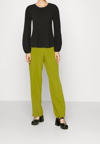 Top lungo a maniche nere a coste con scollatura rotonda, abbinato a pantaloni a gamba larga di colore verde brillante a vita alta e scarpe con piattaforma nere.