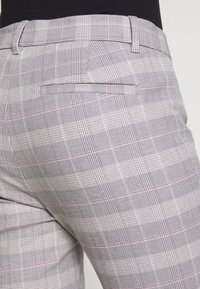 Pantaloni a quadri grigi realizzati in un tessuto testurizzato con linee bianche e rosa, tasche laterali e una tasca posteriore singola. Vestibilità pulita e su misura.