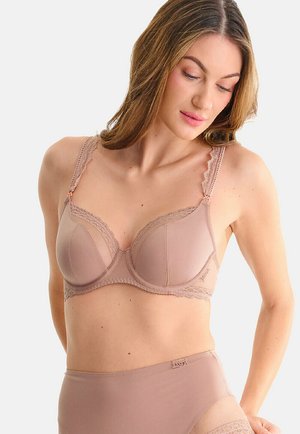 Vrouw die een bijpassende mauve beha en hoogwaterondergoed met kanten details draagt, kijkt naar beneden met haar rechterhand op haar heup.