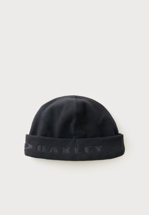 Bonnet en polaire noir avec revers, arborant le logo Oakley embossé sur un fond blanc uni.