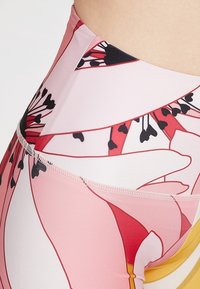 Leggings taille haute en tissu léger et extensible de couleur rose, ornés de grands motifs floraux rouges et noirs, avec une finition lisse et des bordures contrastantes.