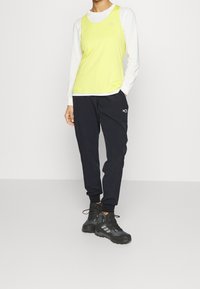 Lätt, ärmlös gul topp som matchas med marinblå tapered byxor och svarta vandringsskor. Har logotyper på toppen och byxorna.