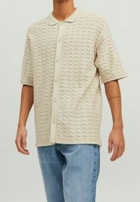 Beige polo shirt met korte mouwen, een gestructureerd patroon, knoopsluiting aan de voorkant en een gladde kraag, gecombineerd met lichtblauwe jeans.