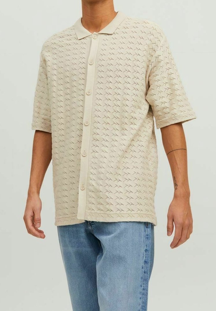 Beige polo shirt met korte mouwen, een gestructureerd patroon, knoopsluiting aan de voorkant en een gladde kraag, gecombineerd met lichtblauwe jeans.