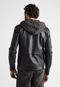 Svart läderjacka med grå huva, med en figursydd design, slät textur och synlig sömnad på baksidan och ärmarna.