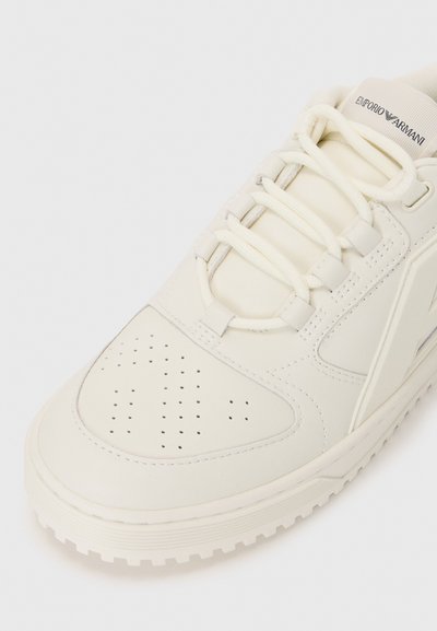 Sneaker in pelle bianca con punta perforata, lacci piatti e suola testurizzata. Marchio visibile sulla linguetta e sul pannello laterale.
