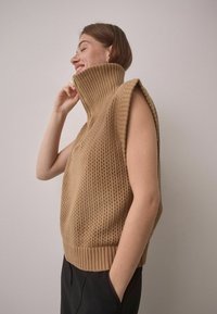 Brown knitted sleeveless pullover with a high ribbed collar, featuring an open weave pattern and a relaxed fit.