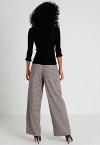 Czarny prążkowany top z rękawami o długości do łokcia w połączeniu z szerokimi spodniami w kratę w kolorach czerwonym, białym i brązowym. Całość dopełniają szpilki.