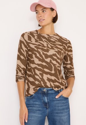 Brun och beige långärmad topp med ett tigerstripesmönster, kombinerad med blå denimjeans. Modellen har också på sig en rosa keps.