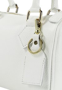 Witte leren handtas met een gestructureerd oppervlak, voorzien van gouden beslag, een afneembare sleutelhanger en een rechthoekig label met stikseldetail.