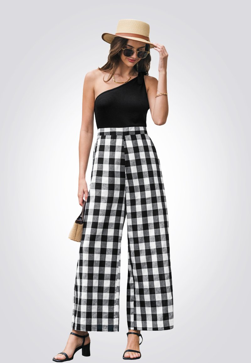 Top negro de un solo hombro combinado con pantalones de cuadros en blanco y negro de pierna ancha. La modelo sostiene un pequeño bolso de mimbre, viste sandalias negras y gafas de sol.