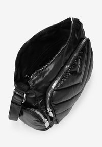 Bolso de hombro acolchado negro con dos cremalleras plateadas, una correa ajustable y un acabado suave y texturizado. El interior es oscuro y espacioso.