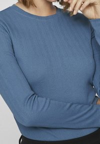 Jersey de manga larga en suave azul tejido con un patrón de diamante texturizado. Escote redondo y puños ajustados, combinado con una parte inferior negra.