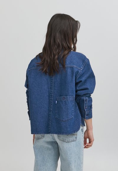 Jeansjacka i mörkblått med en avslappnad passform, knäppta ärmslut och en bröstficka. Har ljus sömnad och en rundad nederkant.