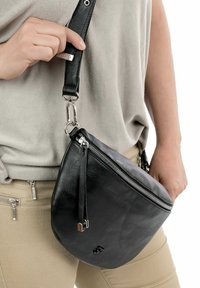 Borsa a tracolla in pelle nera con forma arrotondata, tasca con zip e dettagli in metallo argentato. Cinghia regolabile attaccata.