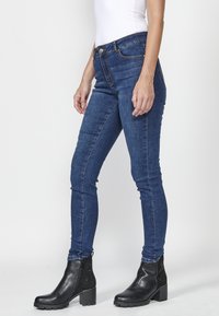 Skinny blue denim jeans with a mid-rise waist, paired with black ankle boots featuring textured accents and a thick, block heel.