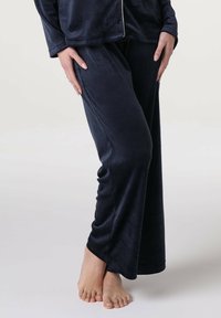 Set da pigiama in velluto blu navy con un taglio largo; presenta maniche lunghe, gambe larghe e una consistenza liscia. Il tocco finale include una leggerissima bordatura.