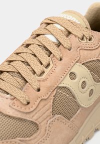 Tenisice u boji breskve s kombinacijom antilopa i mrežastih materijala, teksturiranim vezicama i prepoznatljivim detaljem logotipa sa strane.