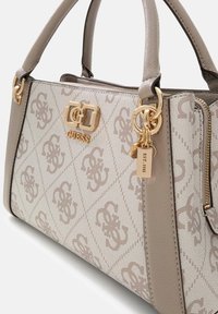 Beżowa torba na ramię z teksturowanego materiału, złotymi okuciami i metalową tabliczką z logo. Posiada wzór w romby i zdobiona jest breloczkiem.