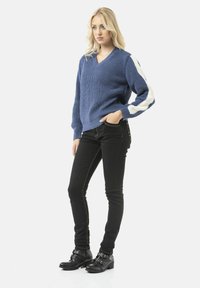 Blauwe gebreide trui met een V-hals en witte gestreepte mouwen, gecombineerd met zwarte jeans en zwarte enkellaarsjes met gesp.