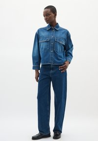 Set di giacca e pantaloni in denim di blu medio. La giacca presenta due tasche sul petto, chiusura con bottone e lievi segni di usura. Pantaloni a gamba dritta.