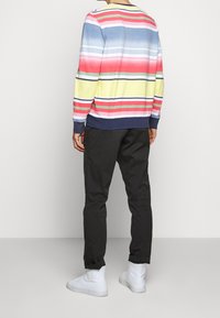 Sweter w wielokolorowe paski w niebieskim, czerwonym, żółtym i zielonym kolorze; czarne dopasowane spodnie; białe trampki typu high-top.