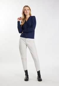 Cardigan tricotat bleumarin cu decolteu în V, închidere cu nasturi și detalii cu deschideri, asortat cu pantaloni albi și cizme negre până la gleznă.