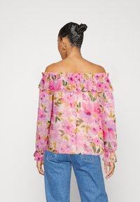 Blouse florale à épaules dénudées en tissu rose transparent avec des accents de volants. Présente des motifs floraux colorés et de longues manches avec des poignets ajustés.