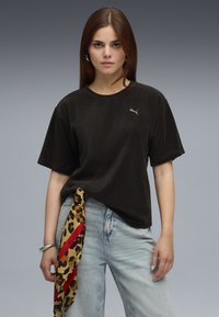 Zwarte corduroy t-shirt met korte mouwen en een ronde hals, voorzien van een klein grijs logo. Gecombineerd met lichtblauwe denim jeans en een panterprint sjaal.
