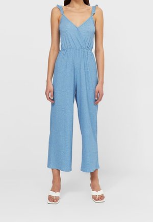 Blauwe, mouwloze jumpsuit met een overslagontwerp en dunne schouderstrikjes; uitgevoerd in een lichtgewicht stof met een subtiel wit stippenpatroon.