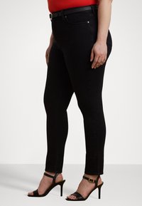 Sorte skinny jeans laget av denim, med en klassisk passform, belte og sidelommer. Brukt sammen med svarte sandaler med høye hæler og stropper.
