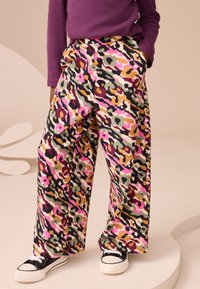 Colorful, wide-leg pants in a camouflage pattern featuring pink, green, and brown hues. Material appears soft, with side pockets and a relaxed fit.