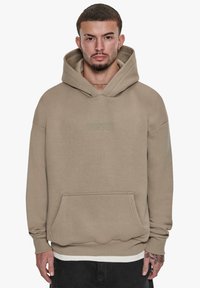 Beige hoodie lavet af blødt stof, med en frontlomme, justerbar hætte og præget "DROPSIZE" logo på brystet.