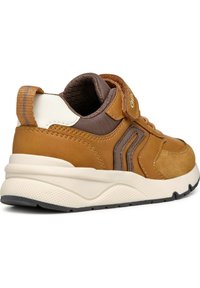 Zapatilla de ante marrón y sintético con un talón blanco en contraste, cuello acolchado y correa ajustable; suela de goma texturizada.