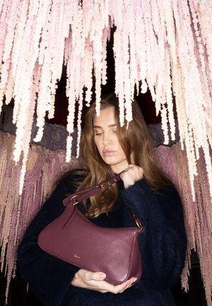 Maroon leather handbag with a curved design, gold hardware accents, and a short strap. Textured finish adds visual interest.