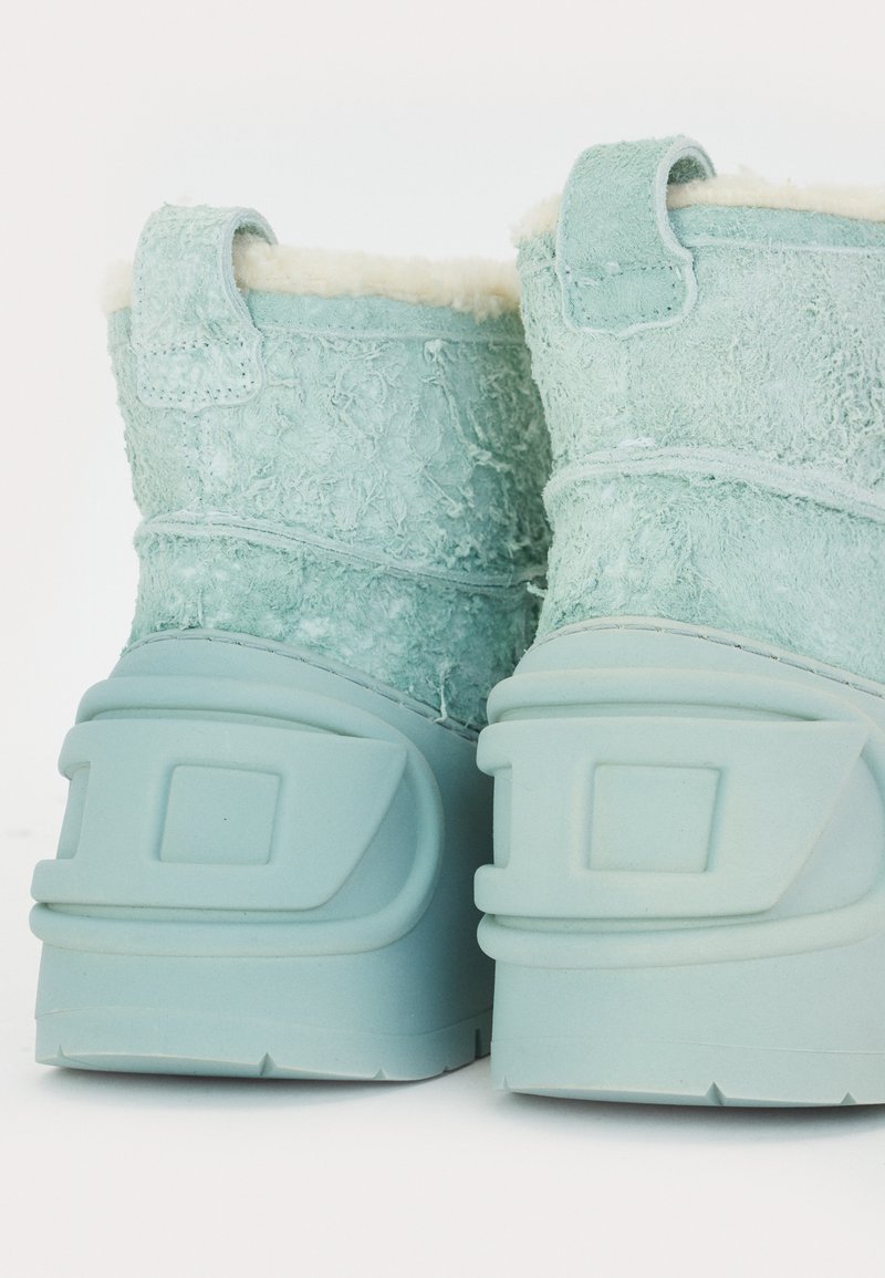 Ein Paar hellblauer Winterstiefel mit strukturierten Wildleder-Oberteilen und dicken Gummisohlen, von hinten vor einem weißen Hintergrund betrachtet.