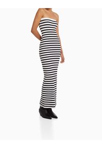 Robe tube rayée noir et blanc en tissu côtelé, silhouette ajustée, longueur cheville, accompagnée de bottes noires à bout pointu.