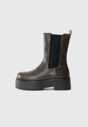 Braune Leder-Ankle-Boots mit elastischen Seiten, robuster schwarzer Plateausohle, runder Zehenpartie und Zuglasche an der Ferse für einfaches Anziehen.