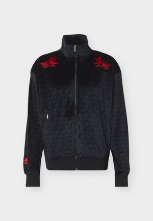 Veste zippée en velours noir avec motif textuel "AFC" sur toute la surface, logos brodés rouges de canon ailé sur les épaules, et logo rouge sur le poignet gauche.