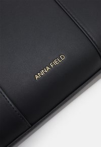 Must must nahkaga kaetud kott sileda tekstuuriga. Esipaneelil on kuldne "ANNA FIELD" logo ja õmblustäiendused.